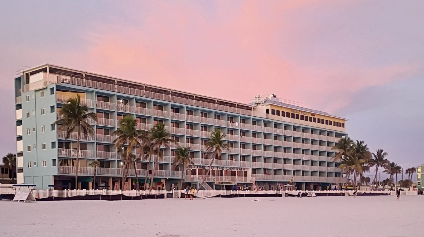 Resort building from the sand, during sunset with orange and pink tones in the sky.